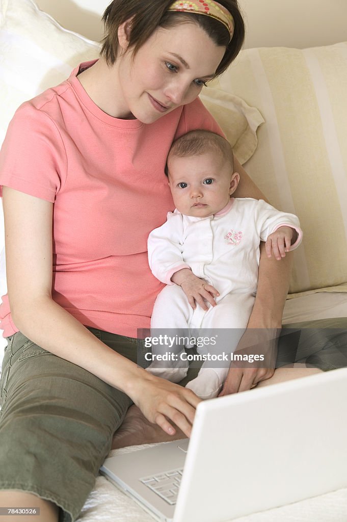 Mother holding baby and typing on laptop