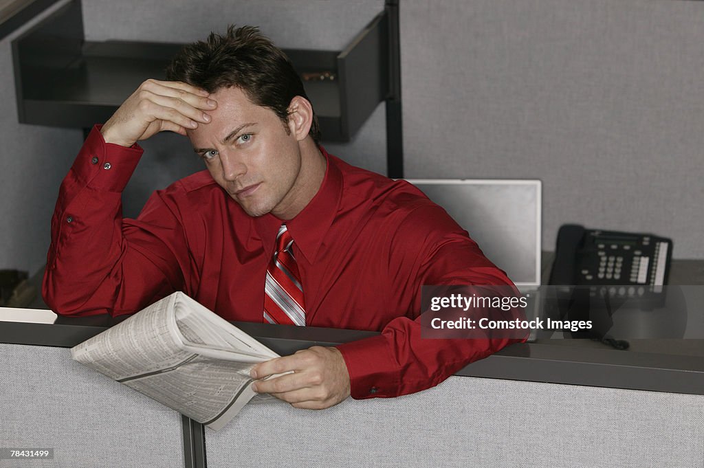 Businessman reading paper in cubicle