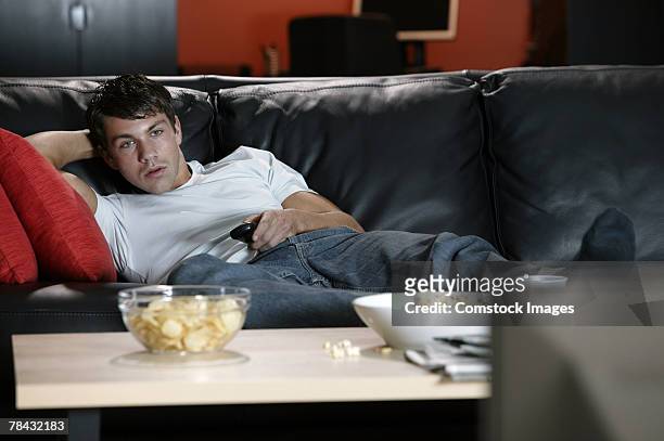 man on sofa watching television - mala postura fotografías e imágenes de stock