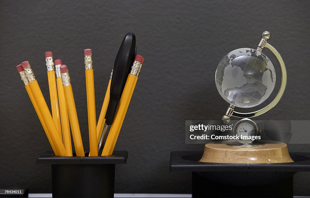 Pencils in cup and globe clock on desk