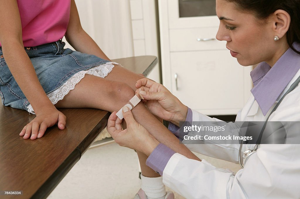 Doctor putting adhesive bandage on girl