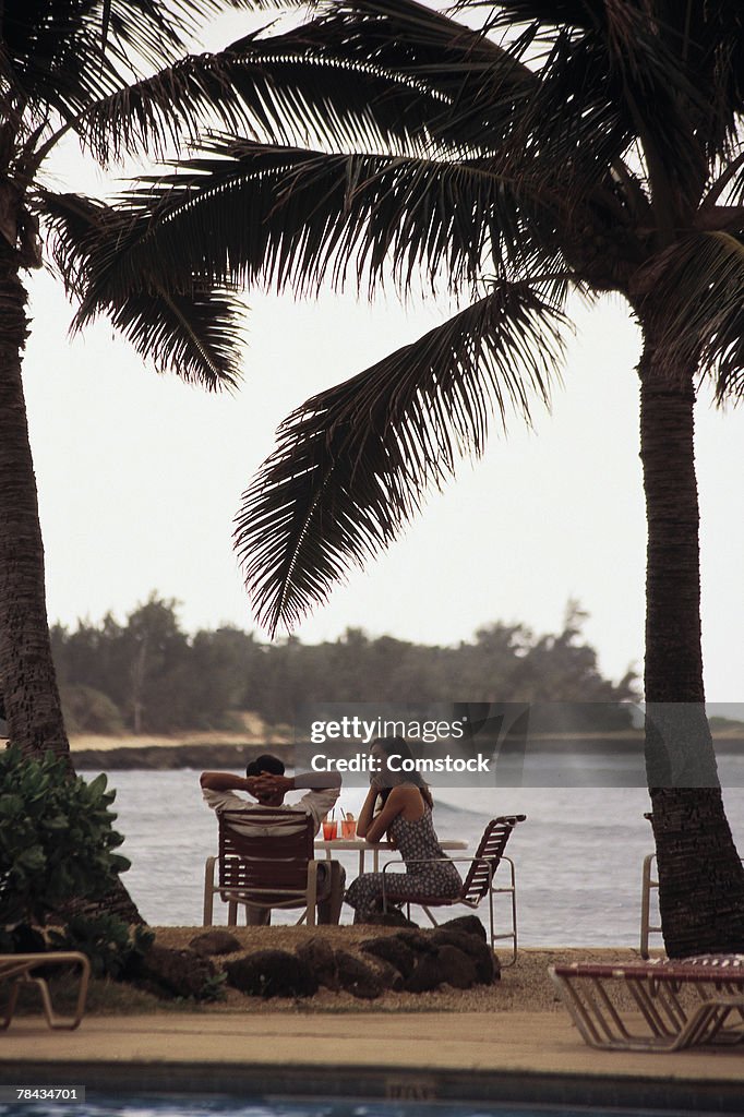 Couple relaxing under palm trees by the water