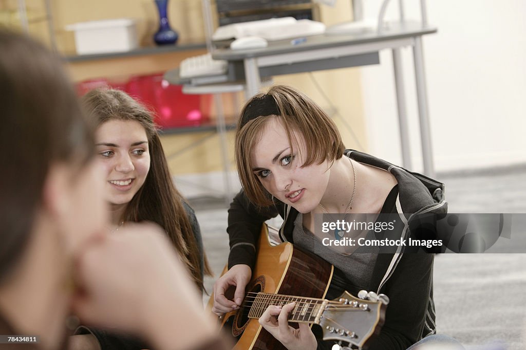 Teenage girl playing guitar with friends