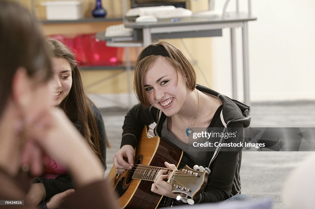 Teenage girl playing guitar with friends