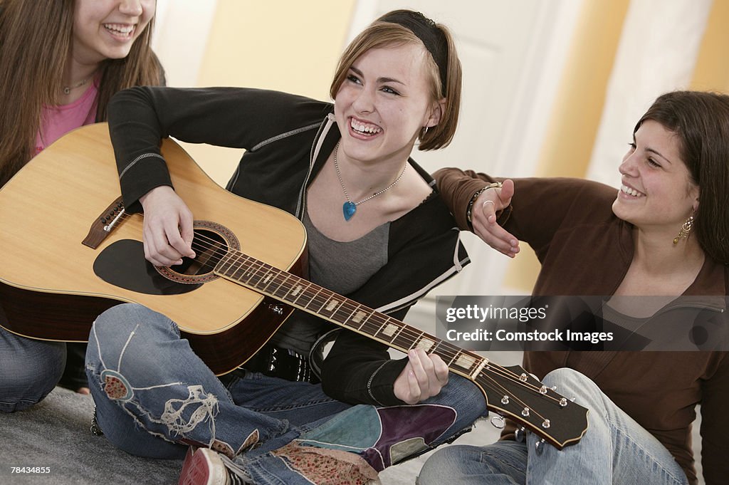 Teenage girl playing guitar with friends