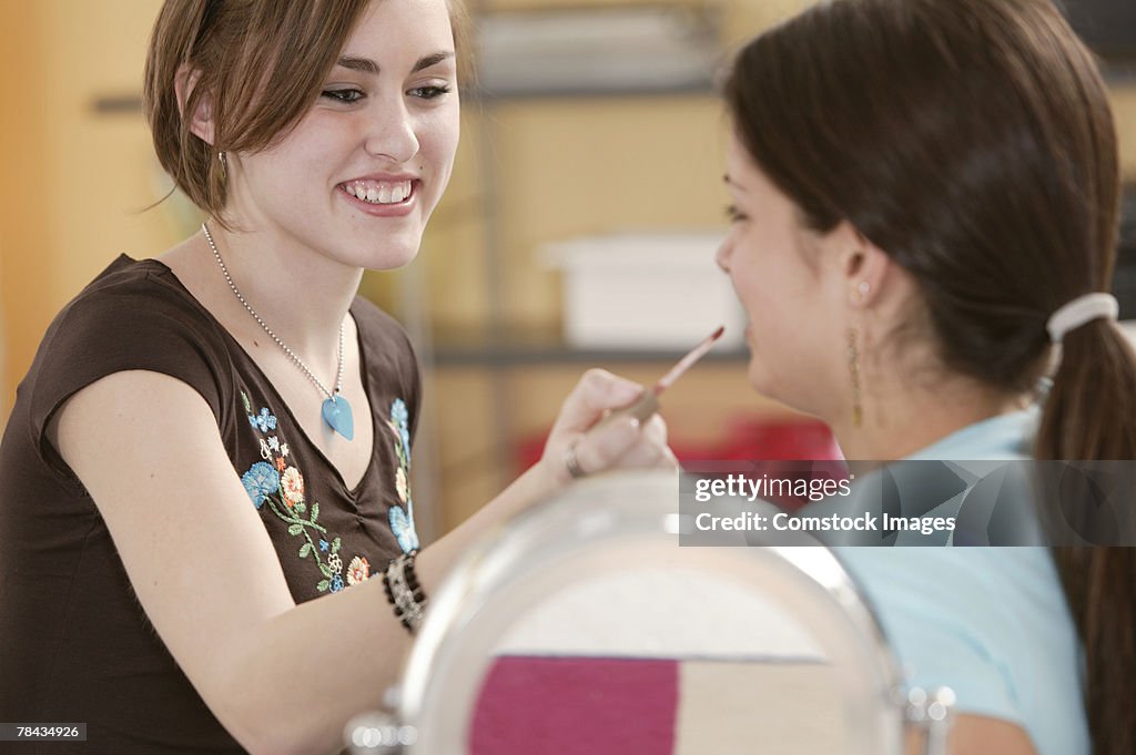 Teenage girl helping friend try on makeup