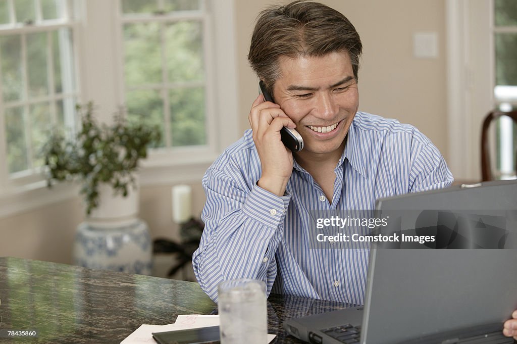 Man using laptop and talking on cell phone