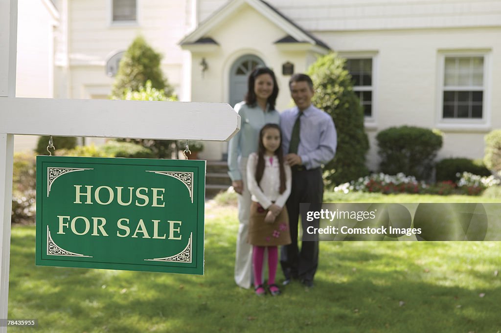 Family standing in lawn with real estate sign