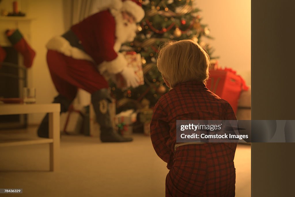 Boy watching Santa put presents under tree