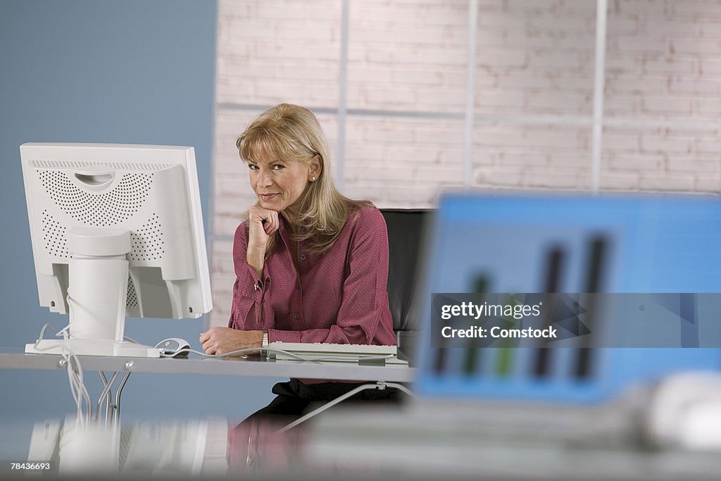 Woman at desktop computer with growth chart on laptop in foreground