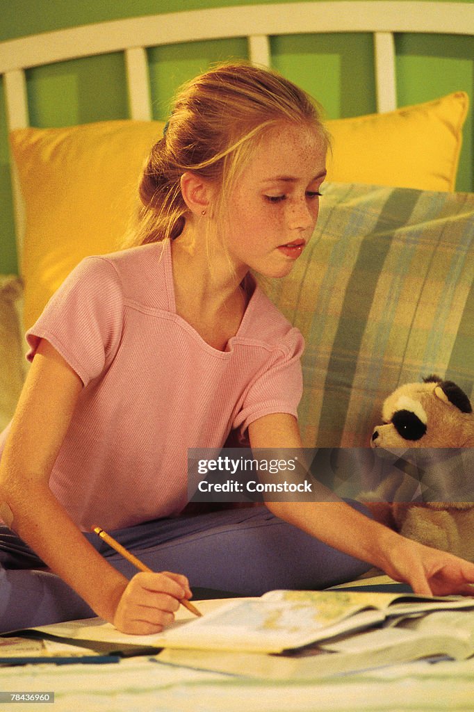 Young girl sitting on bed doing homework