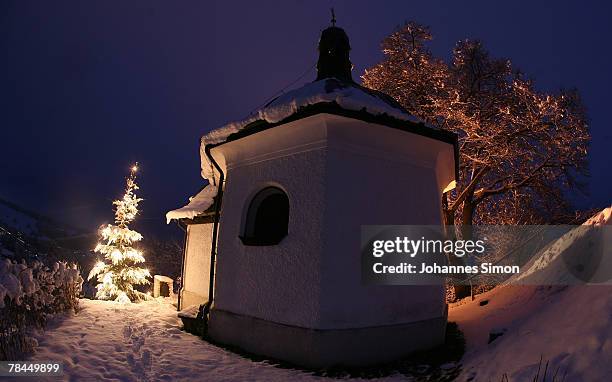 Christmas tree is illuminated in front of an old chapel during dusk on December 13, 2007 in Bad Bayersoien, Germany. Snowfall brought winter back to...