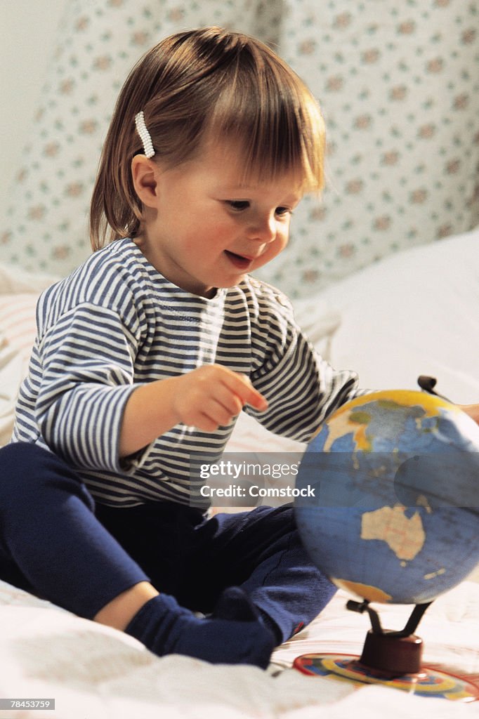 Toddler sitting on bed with a globe
