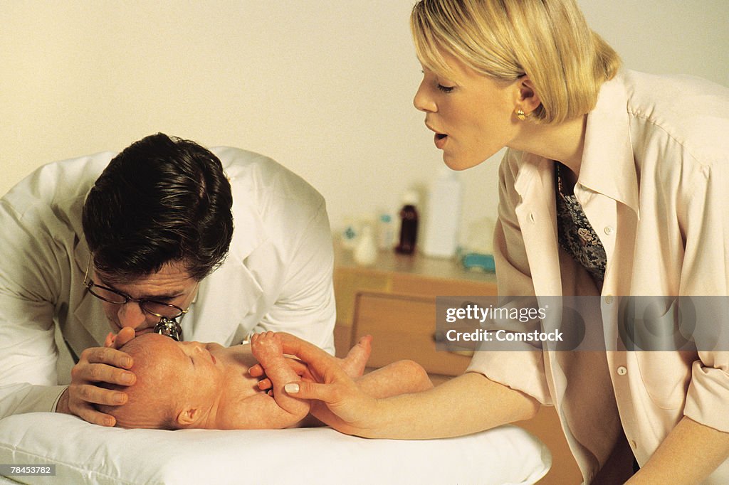 Doctor examines baby while mother gives comfort