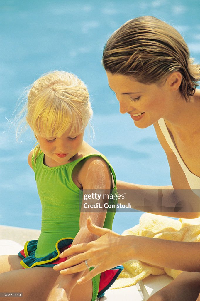 Mother applying suntan lotion to child sitting by pool