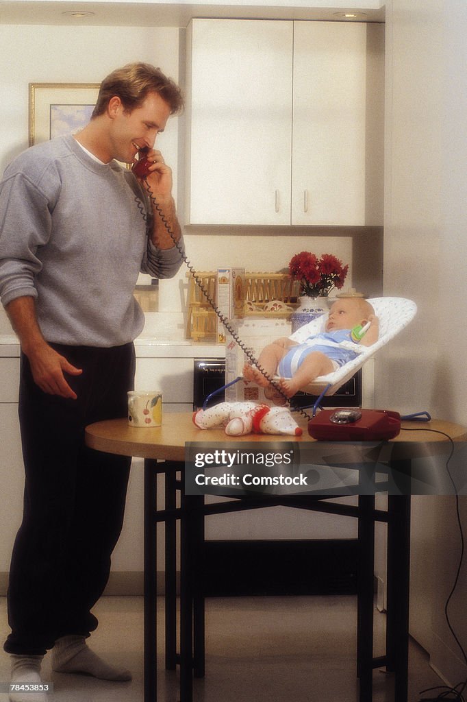Father talks on telephone as he cares for baby