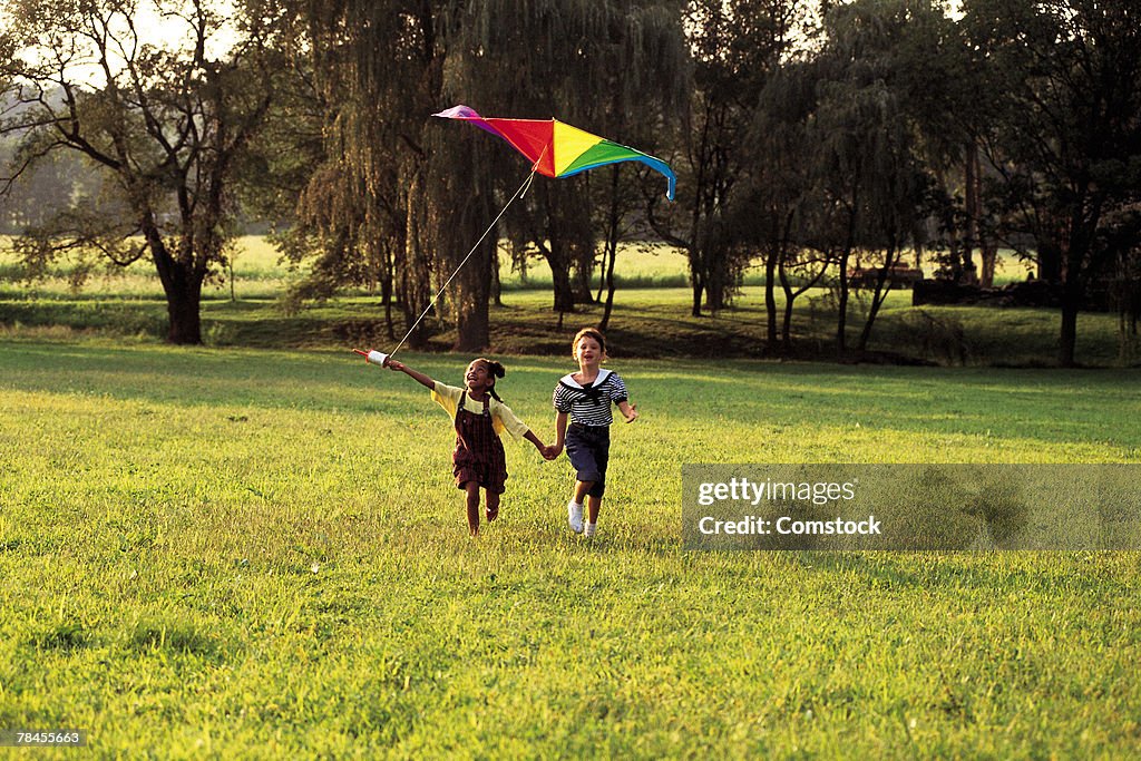 Young girls running in field and flying a kite