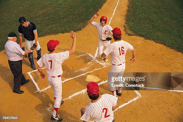 baseball player crossing home plate greeted by teammates - home run stock pictures, royalty-free photos & images