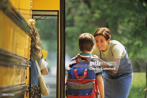 mother sending son off to school at bus stop - school bus fotografías e imágenes de stock