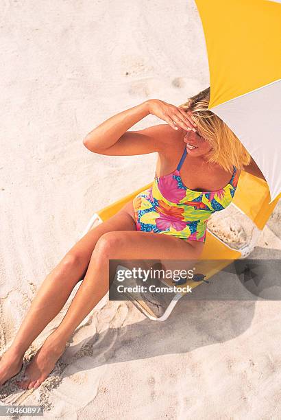 woman sitting in lounge chair at beach - 1990 lounge stockfoto's en -beelden