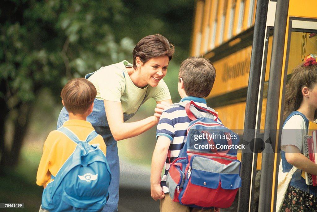 Mother saying goodbye to kids by school bus