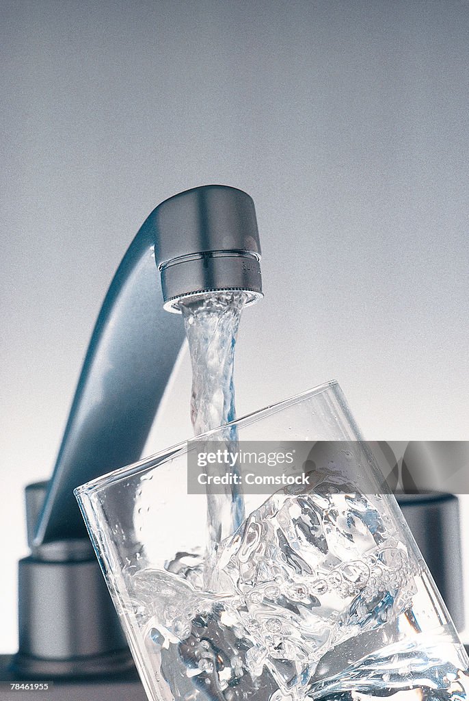 Faucet filling glass of ice with water