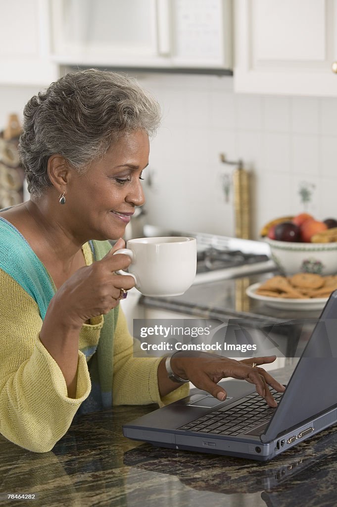 Woman holding coffee cup and using laptop