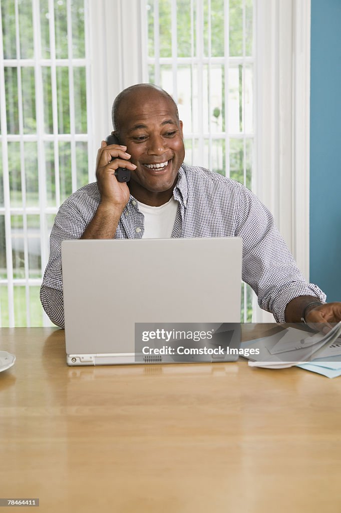 Man with paperwork using cell phone and laptop