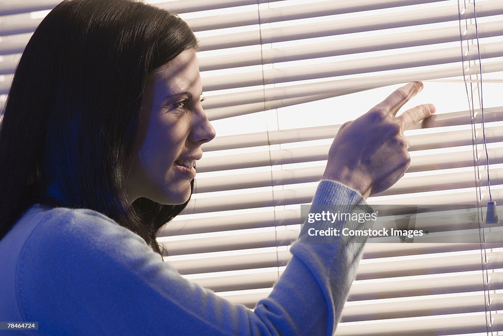 Woman looking out window through blinds