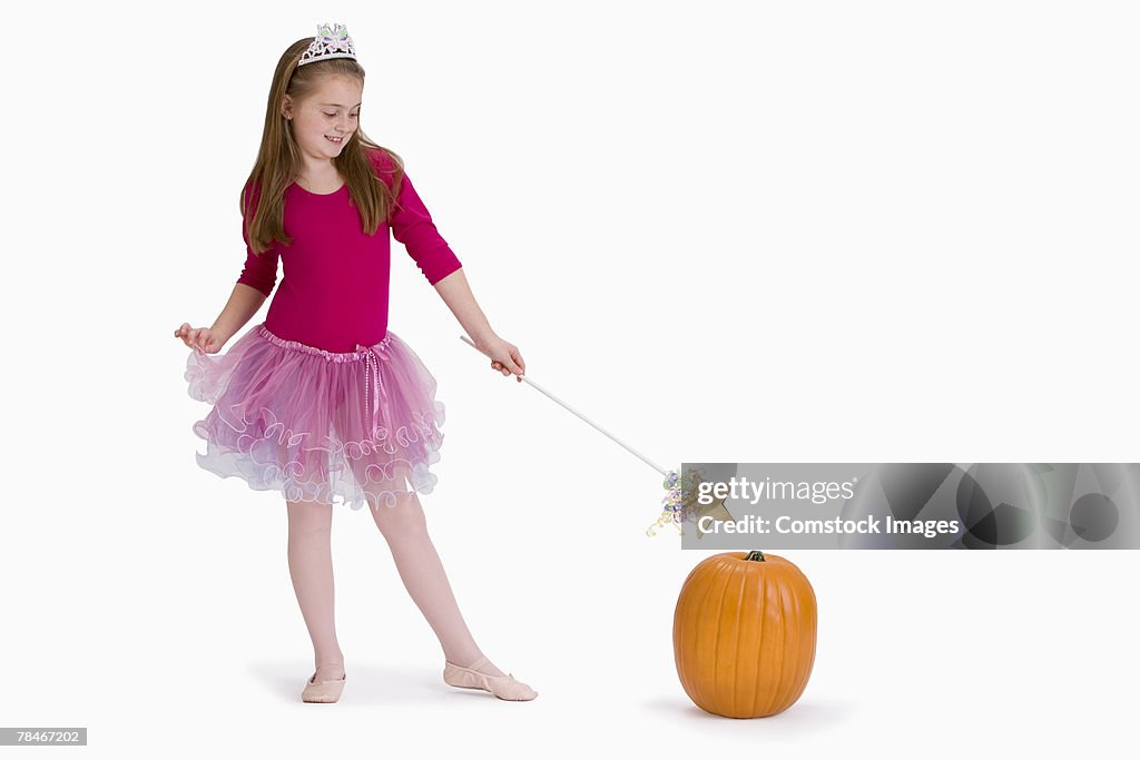 Girl in fairy costume pointing magic wand at pumpkin