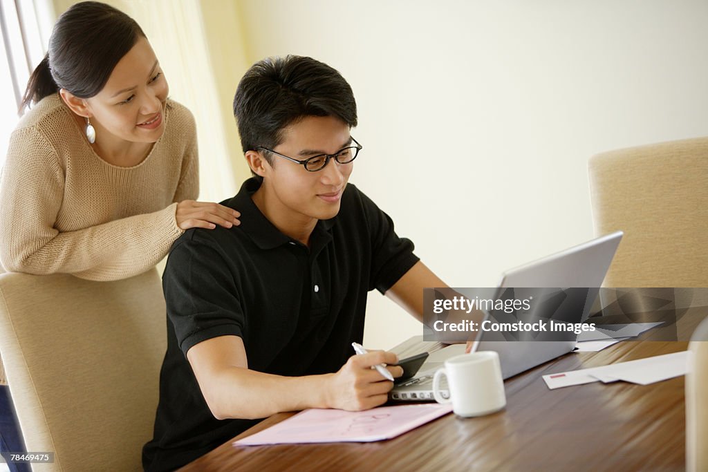 Woman looking over shoulder of man using laptop