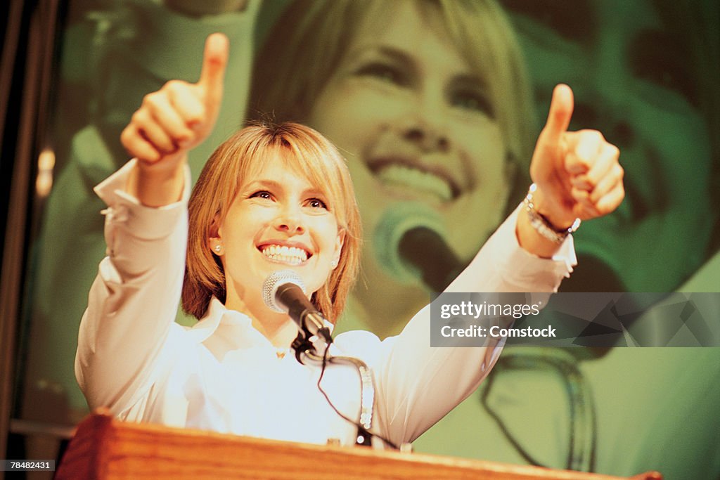 Woman at podium giving thumbs-up