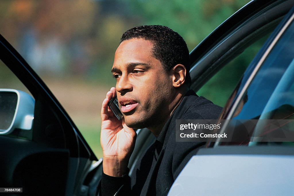 Man sitting in car with open door and talking on cell phone