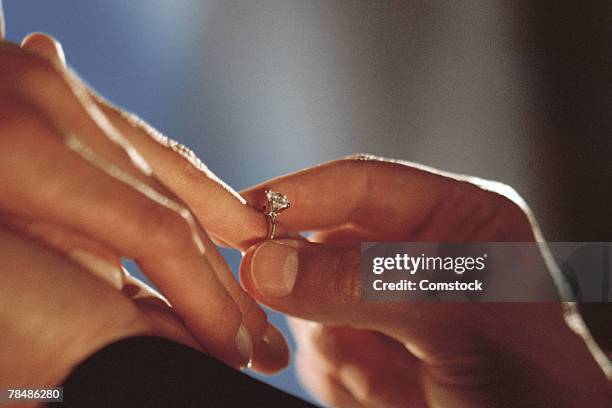 close-up of groom putting wedding ring on bride's finger - woman putting on diamond stock pictures, royalty-free photos & images