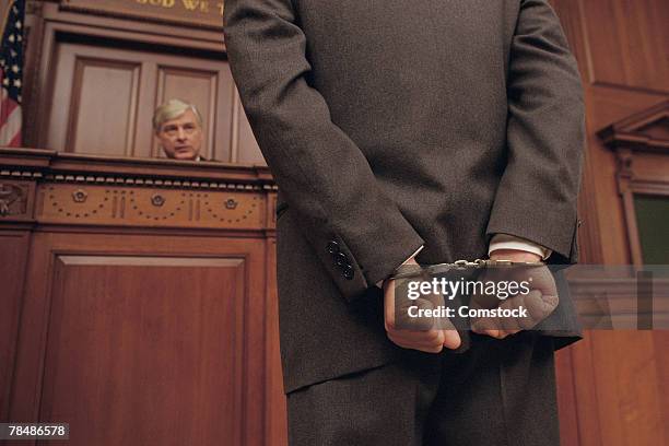 businessman in handcuffs faces judge in court - judge bench stock pictures, royalty-free photos & images