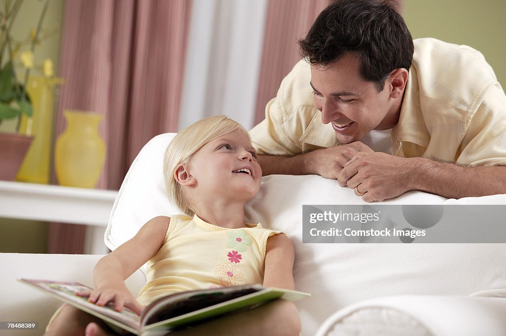 Father watching girl reading a book at home