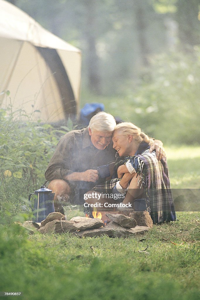 Older couple cuddling by campfire in morning
