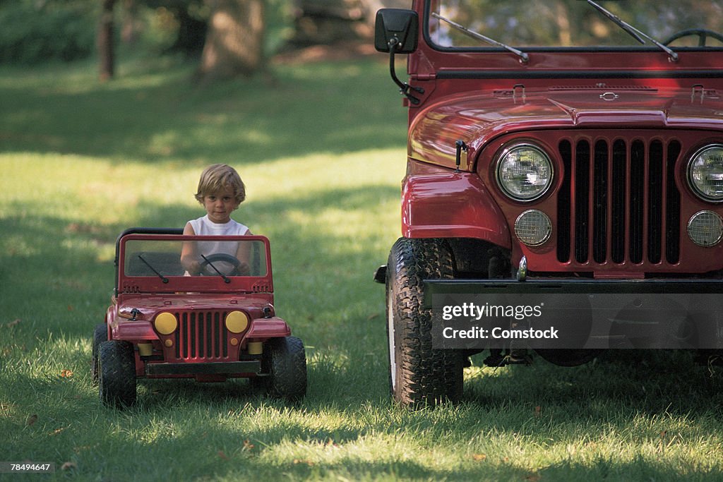 Child driving toy car next to real car