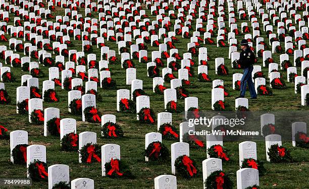 Police officer walks among the more than 10,000 balsam fir wreaths placed by volunteers on the graves of servicemen and women at Arlington National...