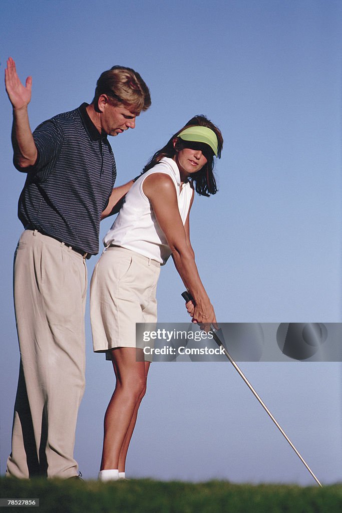Man teaching woman how to swing golf club