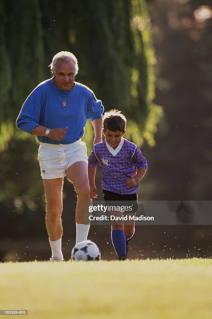 Grandfather playing football in park with boy (7-9)