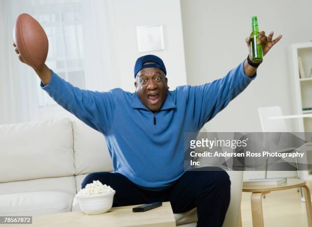 african american man cheering with football and beer - mann anhimmeln stock-fotos und bilder