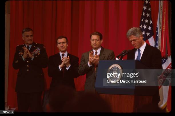 President Bill Clinton stands at a podium while Vice President Al Gore, General Henry Shelton and Secretary of Defense William Cohen clap February...