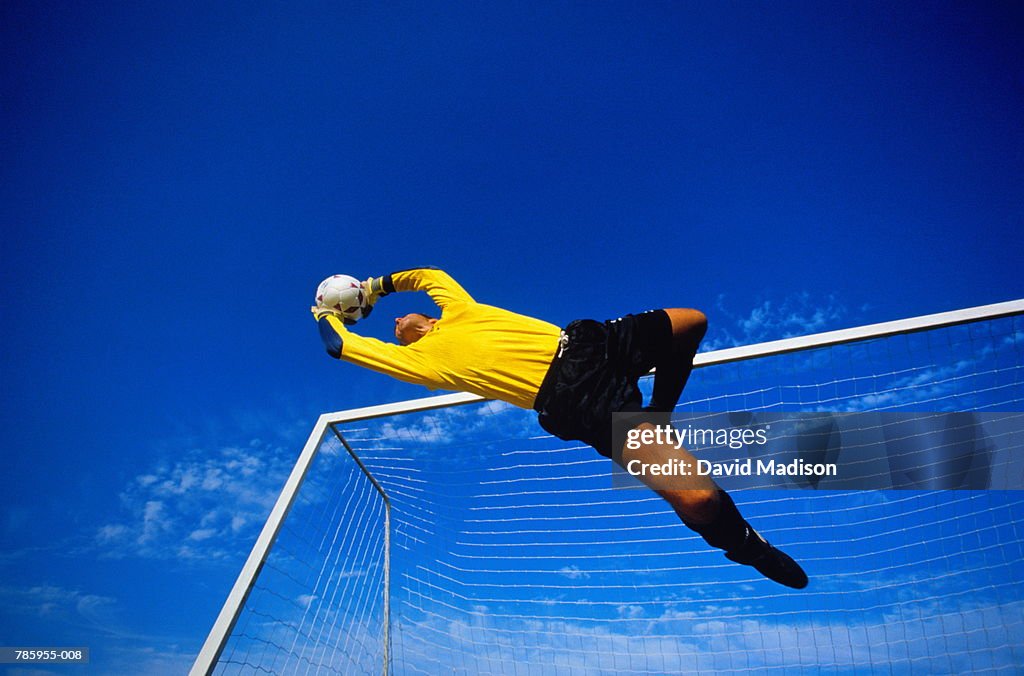 Football, goalkeeper in mid jump, goal in background, low angle view