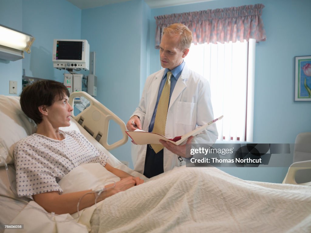 Male doctor talking to female patient lying in hospital bed