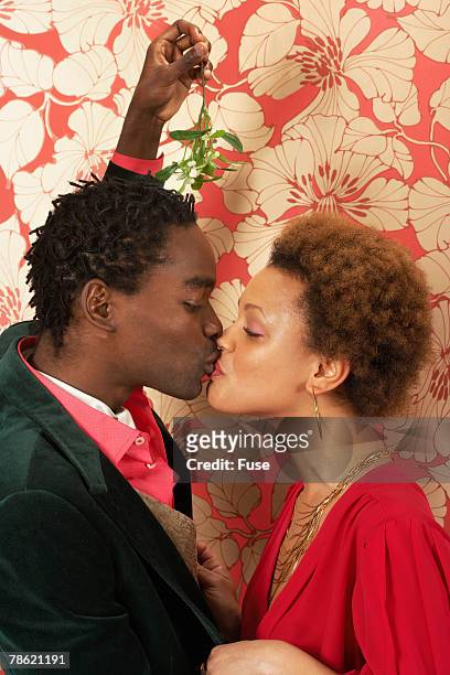 young couple kissing under mistletoe - mistletoe kiss stockfoto's en -beelden