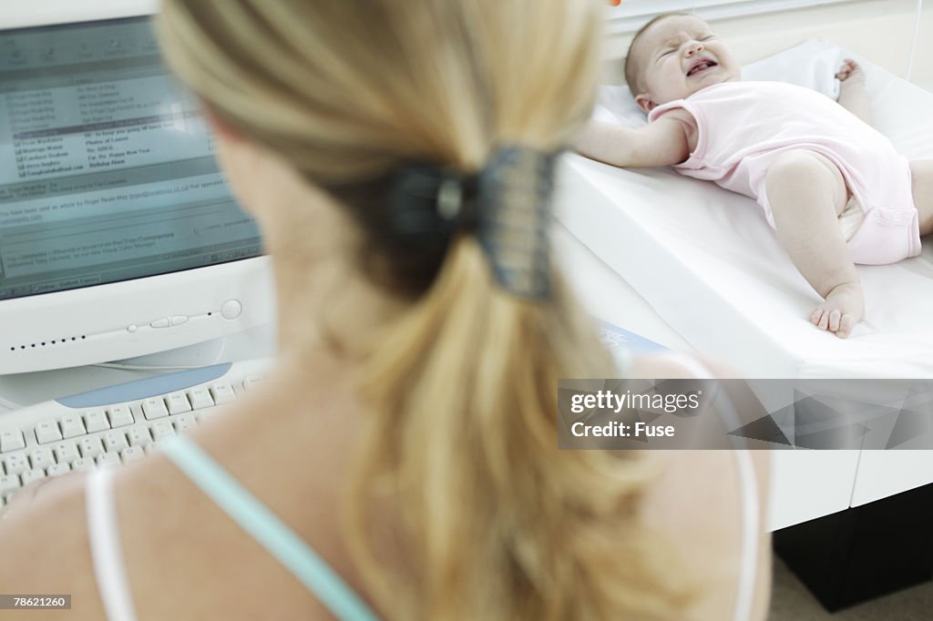 Mother on Computer Next to Crying Baby