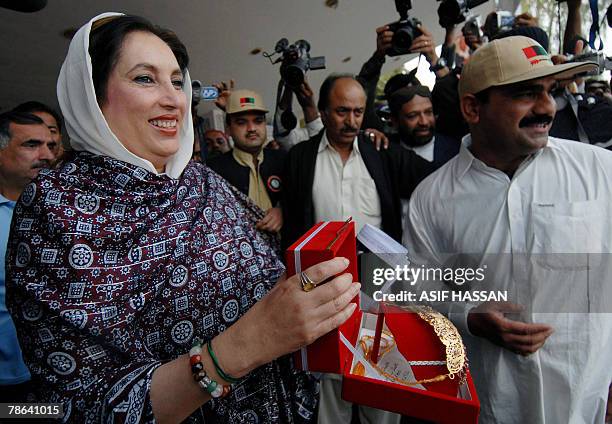 Former Pakistani prime minister Benazir Bhutto smiles after receiving gold jewelry from a party worker during an election campaign meeting in...