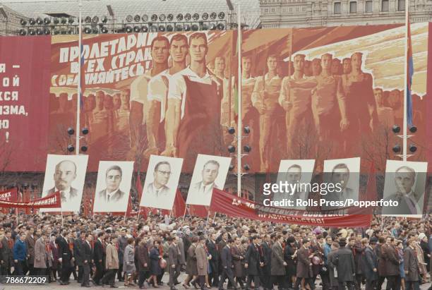 View of spectators, some holding flags, banners and images of Soviet leaders as they watch and applaud fellow citizens marching in the May Day Parade...