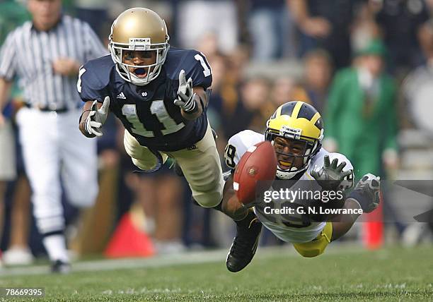 Notre Dame receiver David Grimes and Michigan's Leon Hall stretch out in an attempt to make a catch during action between the Michigan Wolverines and...